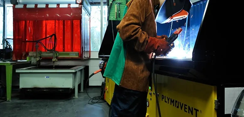 A man welding with a protective mask, gloves and jacket to protect himself from welding spark. He is welding on a Remove The Fume DownDraft Table.