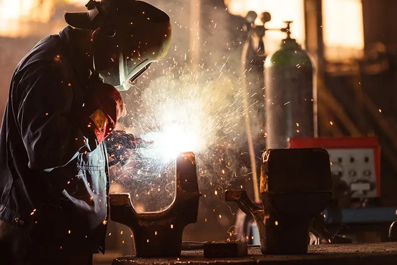 A man welding with a protective mask on while there are welding fumes being generated.