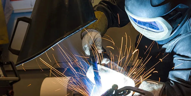 A man welding with a protective mask on and in the background there is a Remove The Fume Fume Extractor who's extraction arm is sucking all the harmful fumes away.