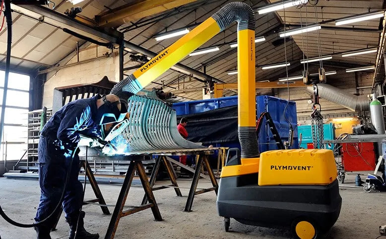 A man welding with a protective mask on a while yellow Remove The Fume fume extractor arm is inhaling all the harmful fume away.
