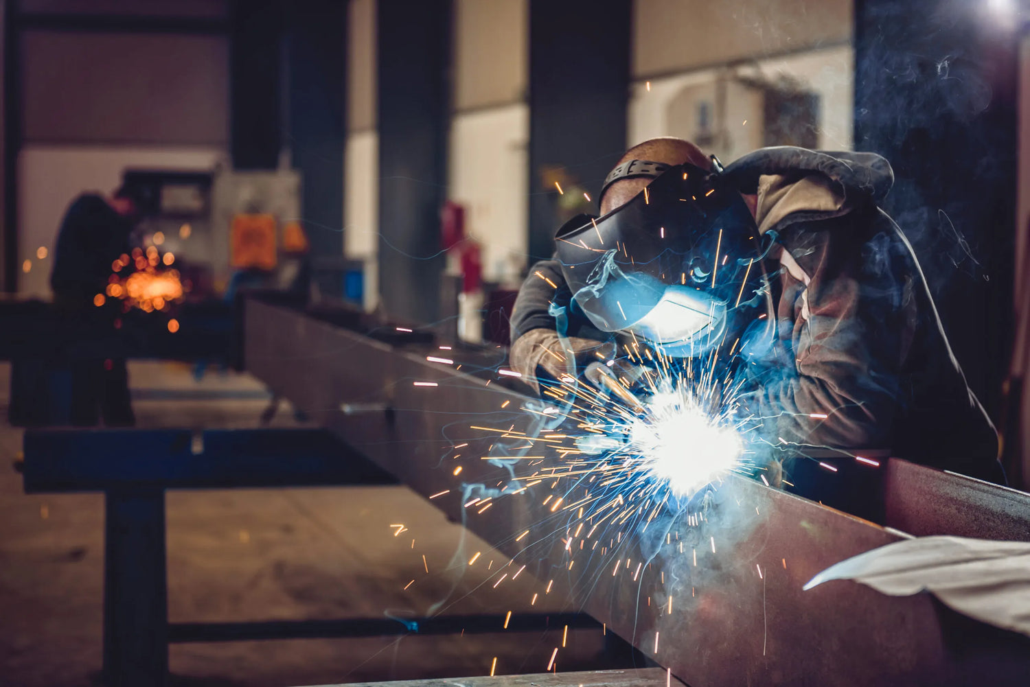 A man welding with his welding mas on and sparks and fumes are being generated.