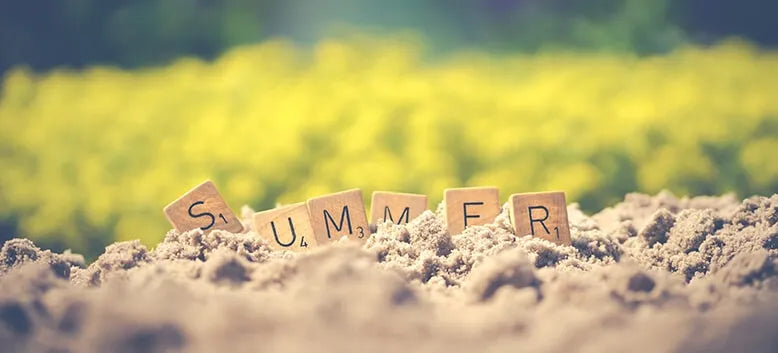 Scrabble pieces spelling the word Summer, stuck in sand.