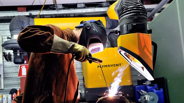 A man welding with a protective mask on a while yellow Remove The Fume fume extractor arm is inhaling all the harmful fume away.