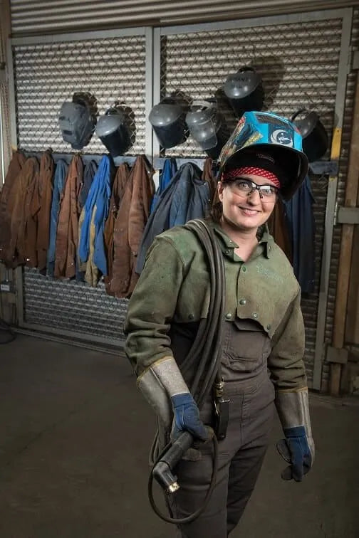 A female welder names Nicole LeClair, is wearing a protective eyewear, gloves and jacket for welding