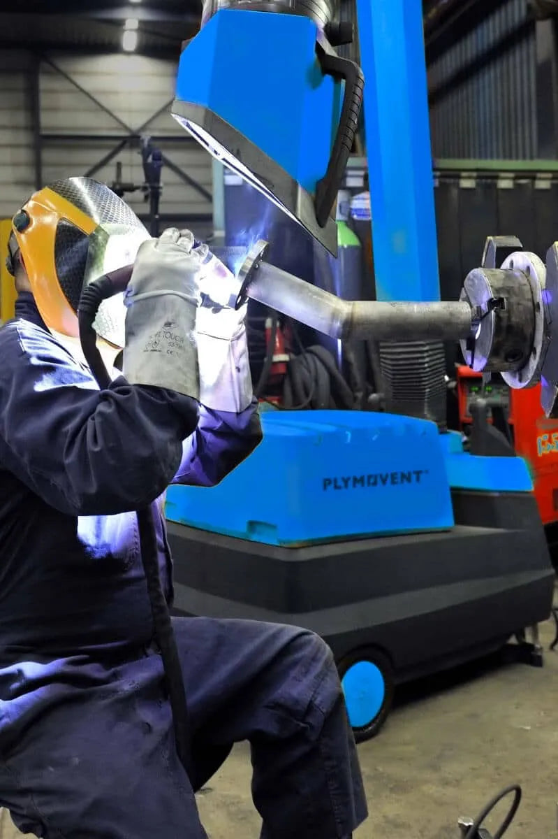 A man welding with a protective mask on and by his side there is a yellow Remove The Fume Fume Extractor who's extraction arm is sucking all the harmful fumes away.