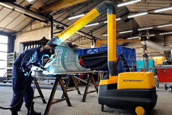 A man welding with a protective mask on and by his side there is a yellow Remove The Fume Fume Extractor who's extraction arm is sucking all the harmful fumes away.