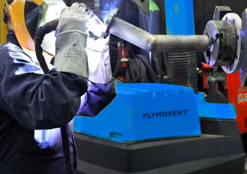 A man welding with a protective mask on and by his side there is a yellow Remove The Fume Fume Extractor who's extraction arm is sucking all the harmful fumes away.