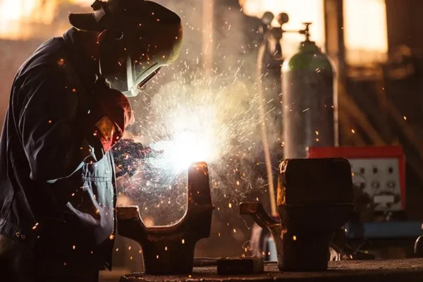 A man welding with a protective mask on while there are welding fumes being generated.