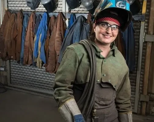 A female welder names Nicole LeClair, is wearing a protective eyewear, gloves and jacket for welding