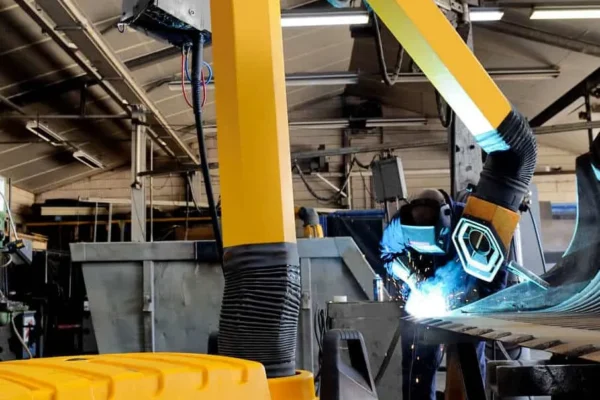 A man welding with a protective mask on a while yellow Remove The Fume fume extractor arm is inhaling all the harmful fume away.