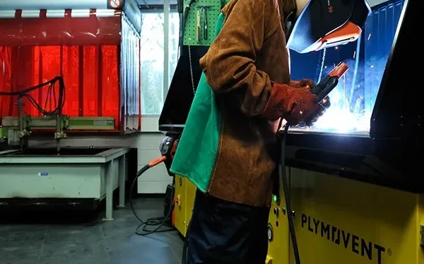 A man welding with a protective mask, gloves and jacket to protect himself from welding spark. He is welding on a Remove The Fume DownDraft Table.