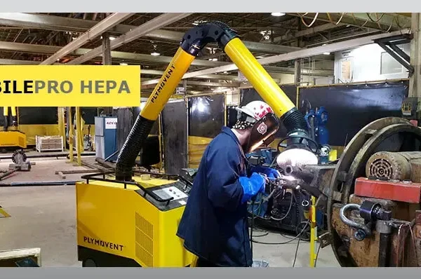 A man welding with a protective mask on a while yellow Remove The Fume fume extractor arm is inhaling all the harmful fume away.