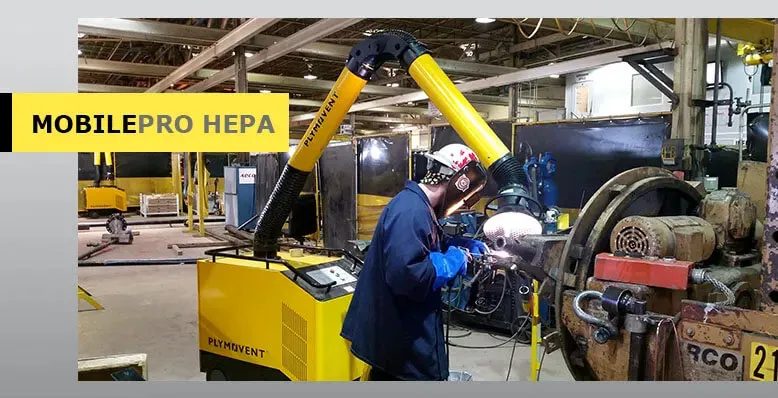 A man welding with a protective mask on a while yellow Remove The Fume fume extractor arm is inhaling all the harmful fume away.