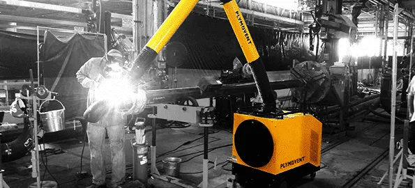 A man welding with a protective mask on a while yellow Remove The Fume fume extractor arm is inhaling all the harmful fume away. The image is black and white but the fume extractor is in yellow color