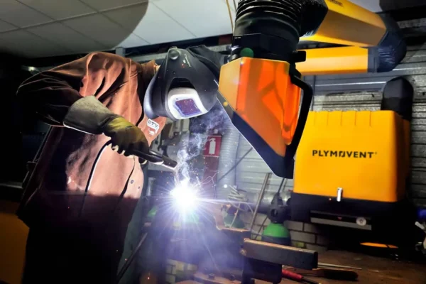 A man welding with a protective mask on a while yellow Remove The Fume fume extractor arm is inhaling all the harmful fume away.