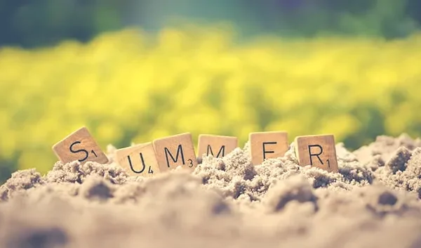 Scrabble pieces spelling the word Summer, stuck in sand.